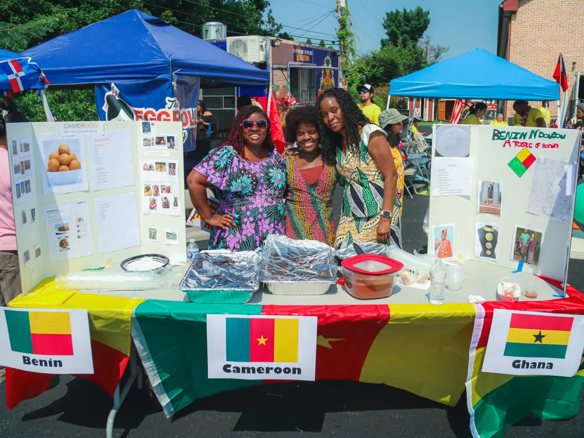 Women standing beside cultural displays and flags at an outdoor festival